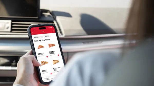 A photo of a a hand holding a mobile phone. The phone shows an app that says "Pizza by the slice. Pepperoni slice, mega meat pizza slice, supreme pizza slice, cheese pizza slice."