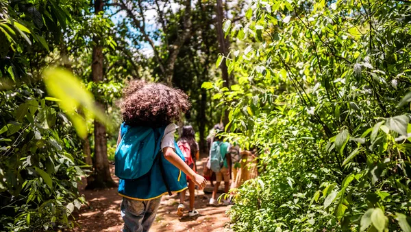 A group of adolescents is pictured hiking a trail through a forest.