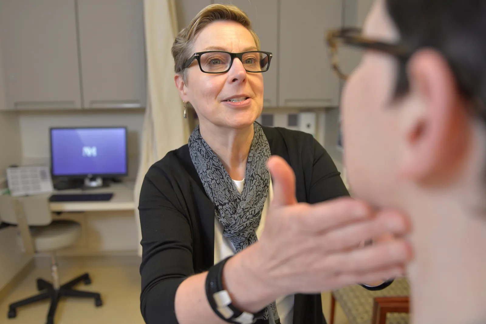 A person feels the under jaw of another person in a doctor&#x27;s exam room.