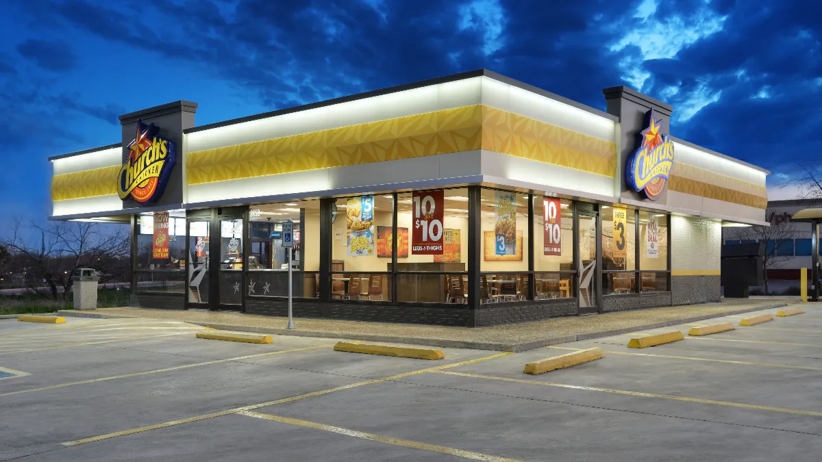 An exterior image of a white restaurant with a yellow decoration and signs that say Church's Chicken