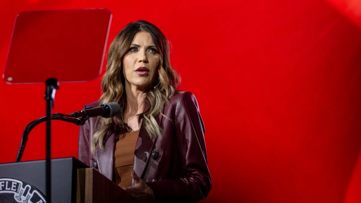 South Dakota governor Kristi Noem speaks at a podium against a red background.