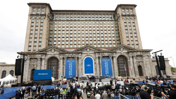 A crowd of people gather on the front steps of an older multistory building decorated with blue banners.