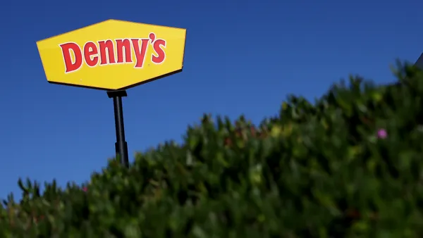 A photograph of a Denny's sign over some trees.