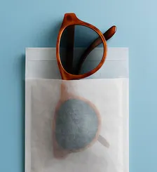 A pair of sunglasses is encased in a translucent paper pouch.