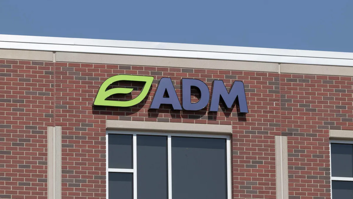 A close-up view of a red brick building with a large "ADM" logo mounted near the roofline, featuring a green leaf icon and dark blue letters.
