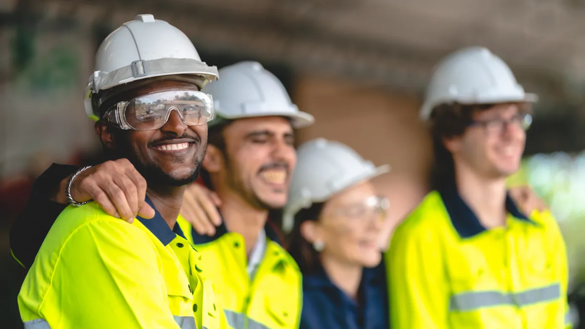 construction workers wearing hard hats smile and stand together