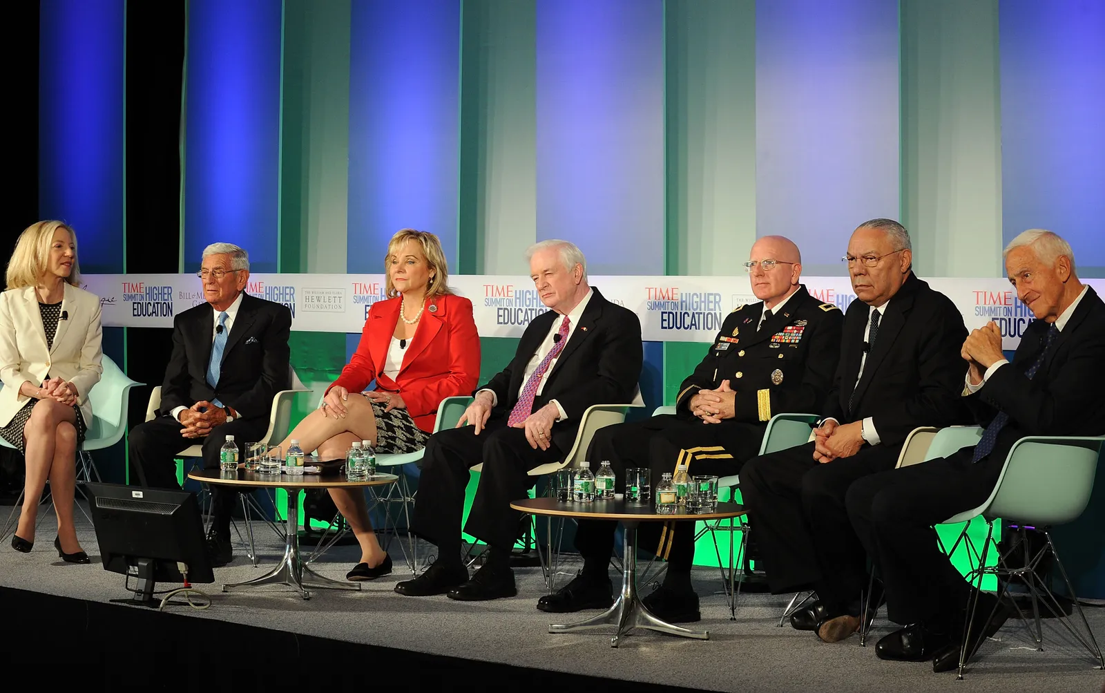 Panelists sit on stage in front of a green and blue background.