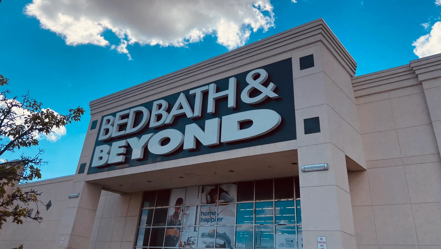 A Bed Bath & Beyond sign against a blue sky with puffy white clouds.