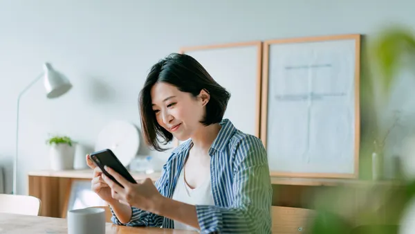 Person managing financial bill payment with smartphone and credit card in the living room at home.