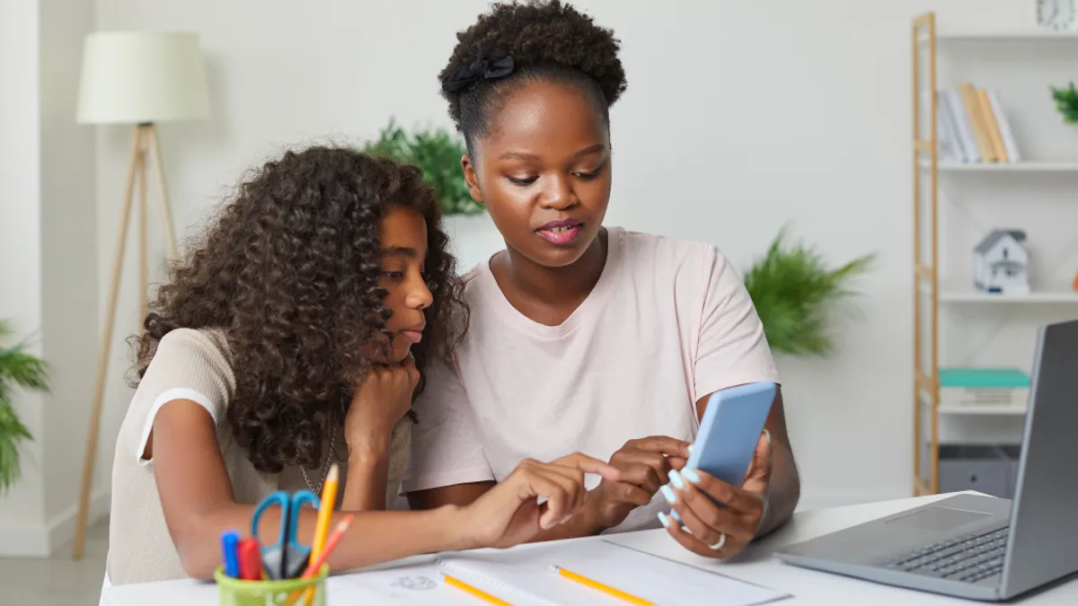 A parent helps her teenage daughter complete her school homework while using her smartphone.