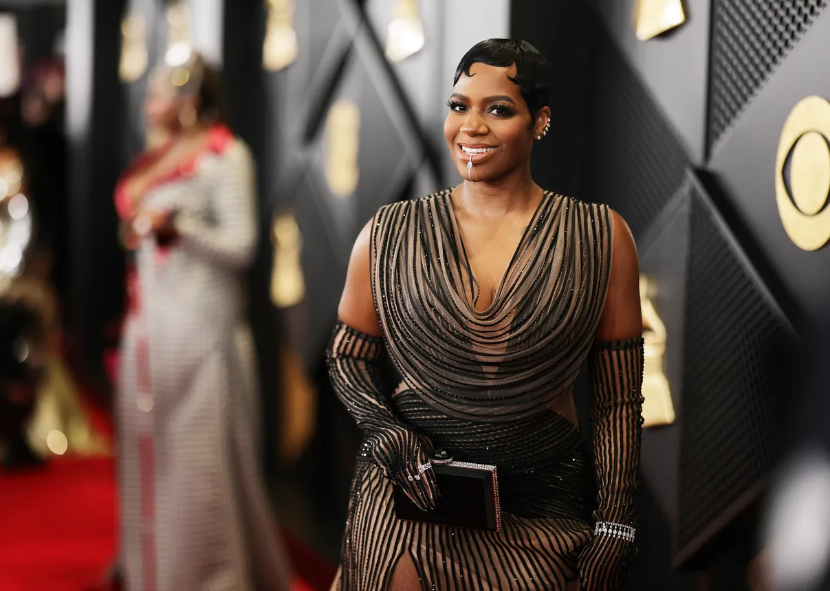 Fantasia holds a small clutch while wearing an illusion gown and smiling at the camera.