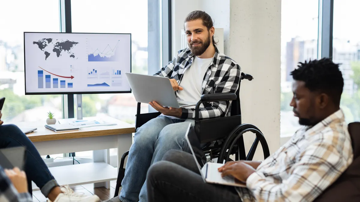 A man in a wheelchair faces a group of people, contributing to the dialogue in a collaborative setting.