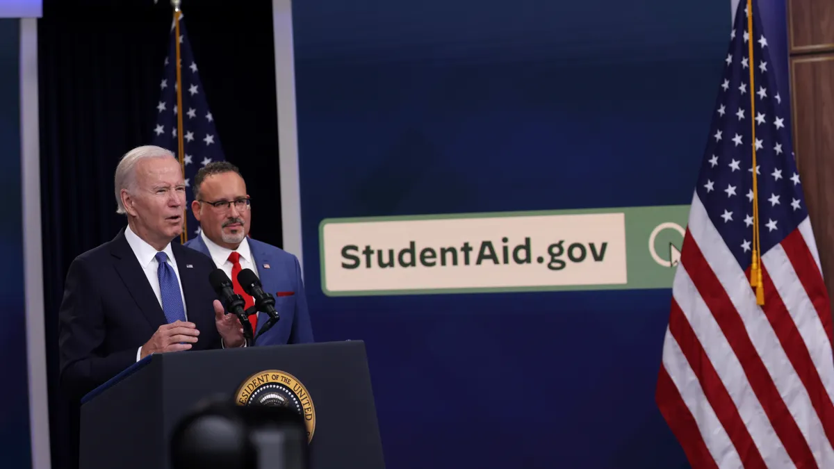 President Joe Biden speaks at a podium while Education Secretary Miguel Cardona stands in the background.