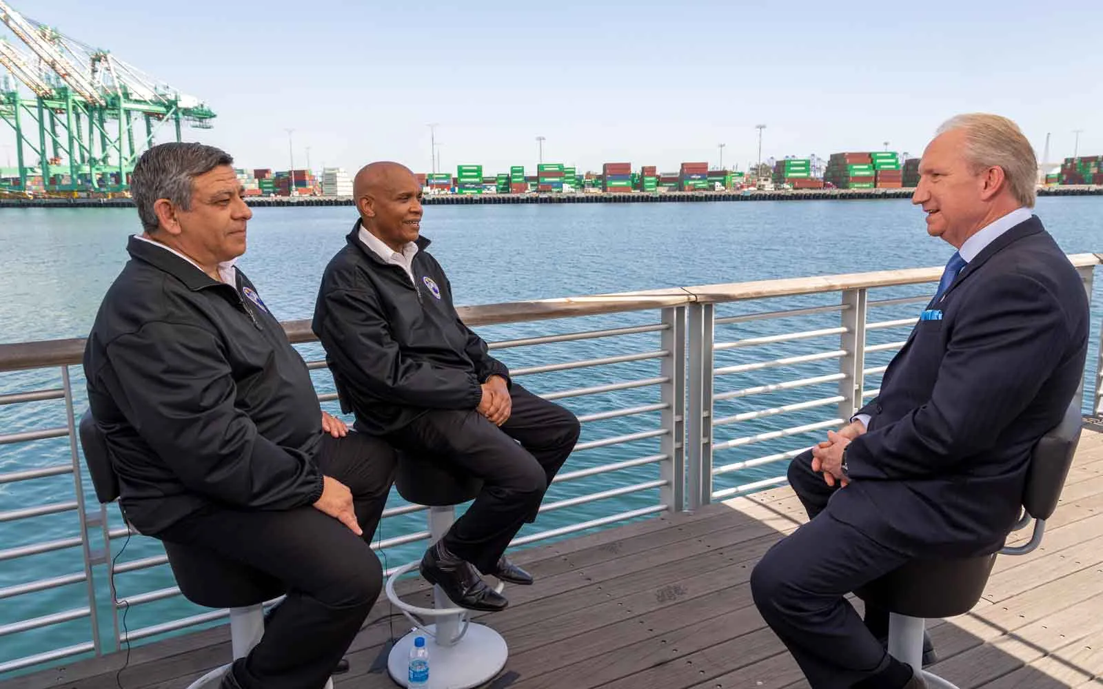 POLA Director sits across from ILWU President and Committeeman in an interview, with the port in the background