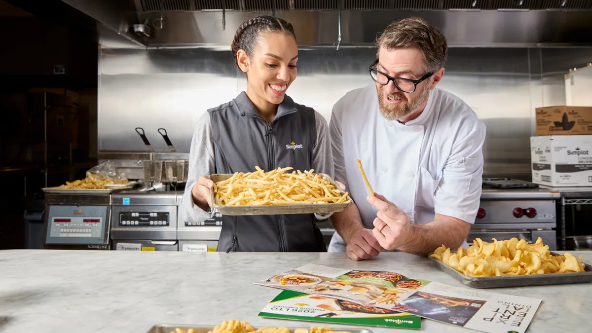 A chef and a kitchen worker present a tray of french fries in a commercial kitchen.