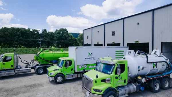 Several kinds of trucks, like box and vacuum, are lined up in front of bays in a large industrial shed. They all have Momentum Environmental branding.