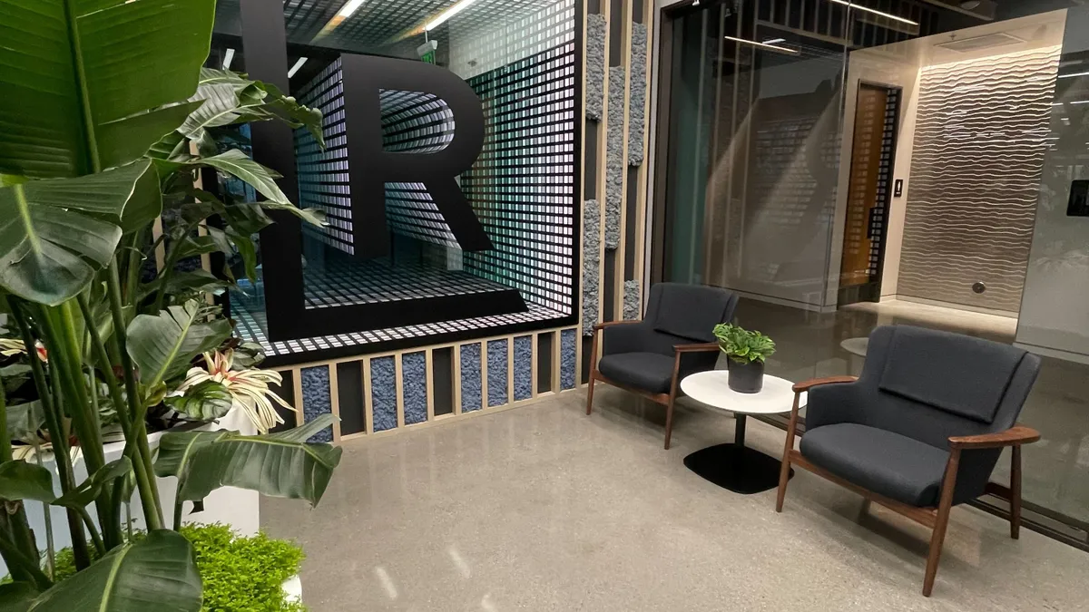 A black letter R inside a white and square consist of blue-green cubes in a lobby.