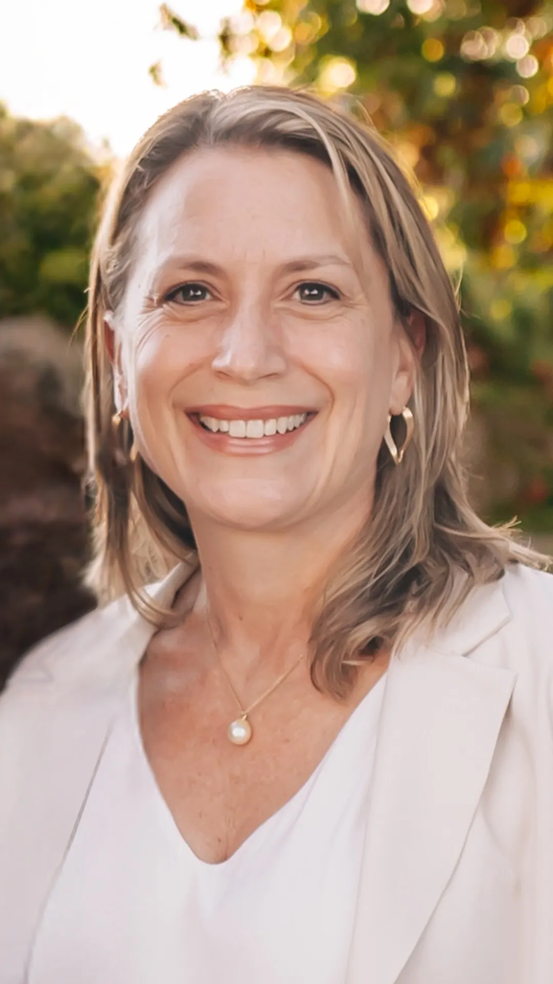 A smiling woman in front of green foliage.