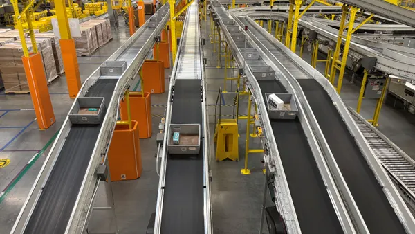 Gray trays with items are being transported on conveyor belts in a warehouse.