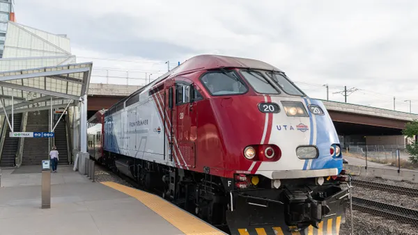 A red, white and blue locomotive and train at a station with a person walking toward an escalator.