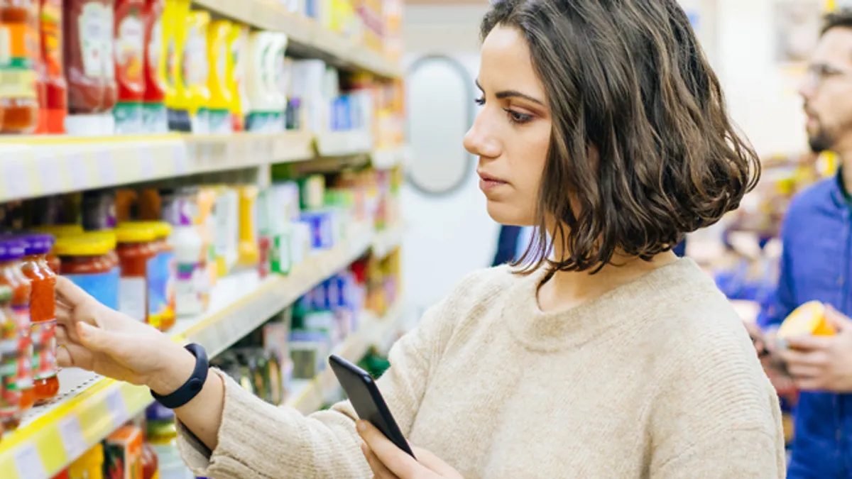 Woman holding smartphone and choosing goods in supermarket.