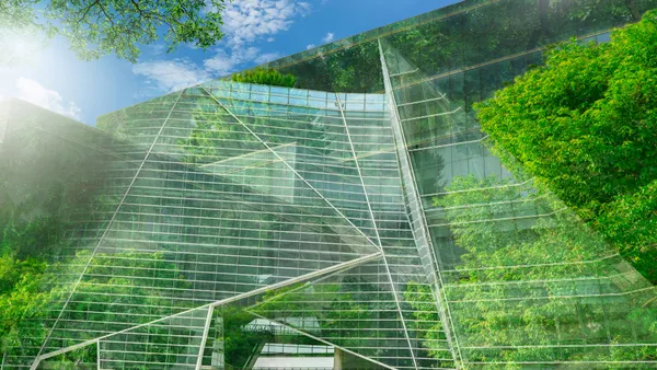 A facade of a sustainable glass office building with a tree for reducing carbon dioxide.