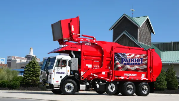 A red waste collection truck with the Patriot Disposal logo on the side in a parking lot