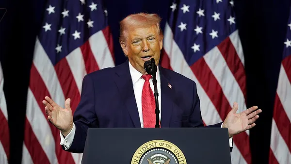 Trump stands at a podium with American flags in the background.