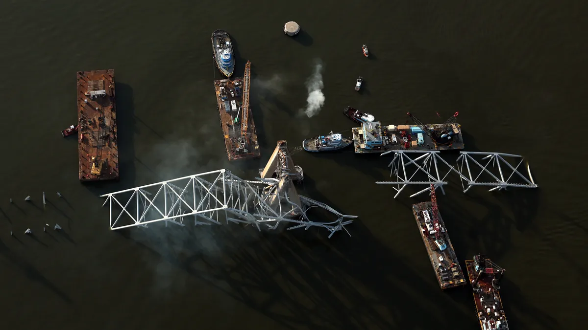 In an aerial view, salvage crews use cranes and barges to remove bridge wreckage from the a cargo ship.