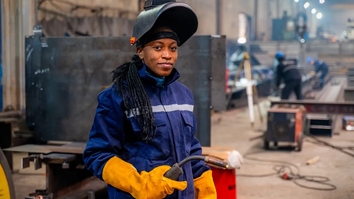 A Black girl in a welding uniform and helmet practices her skills in a career learning program.