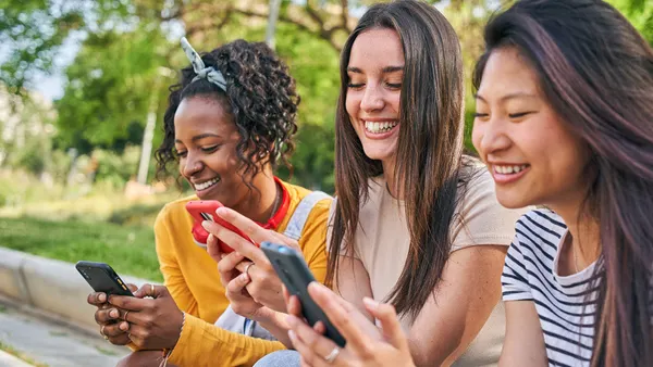 Young adults outside on their phones smiling