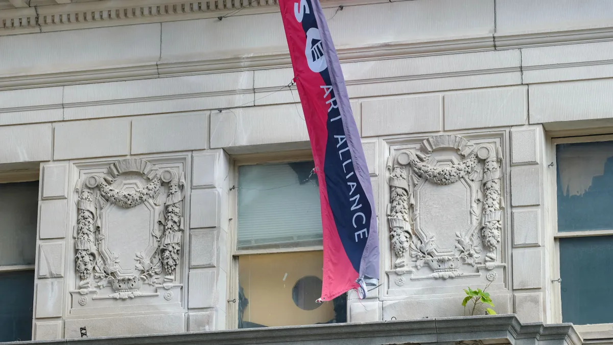 Photo of a red and blue flag in front of a stone building.