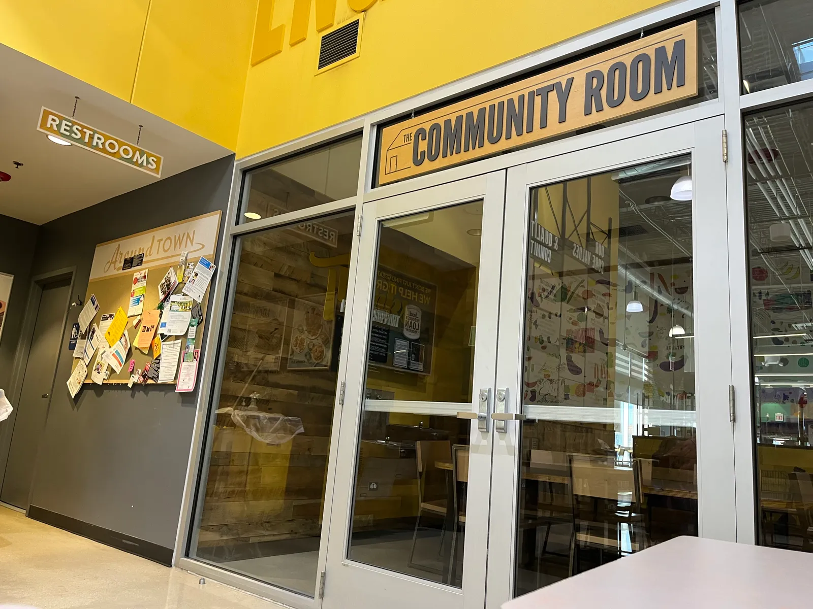 Inside a store, a bulletin board with local event flyers and doors to the "Community Room."