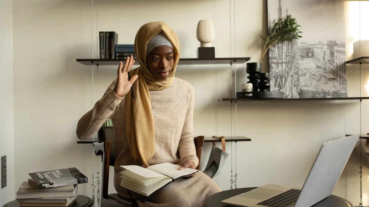 A Muslim person in a hijab looks at their laptop screen