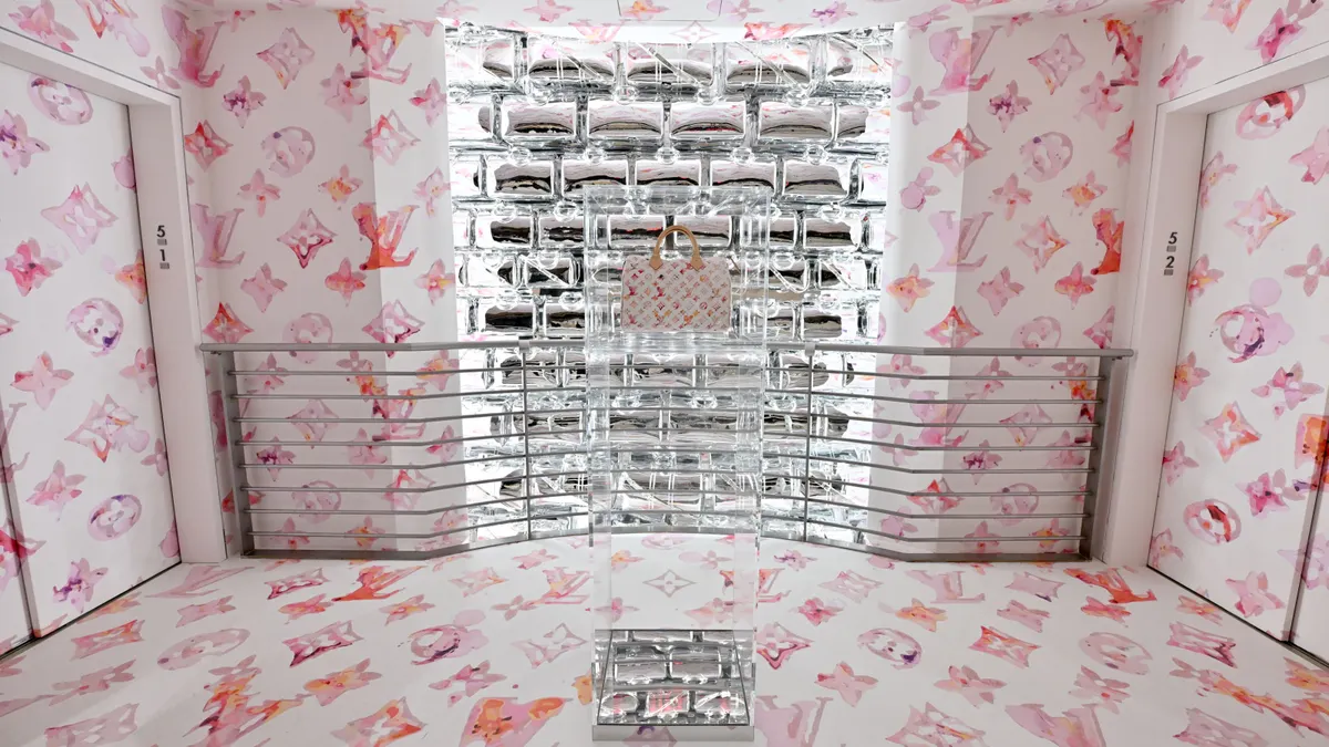 A handbag on display against a pinkish background featuring the logo of Louis Vuitton.