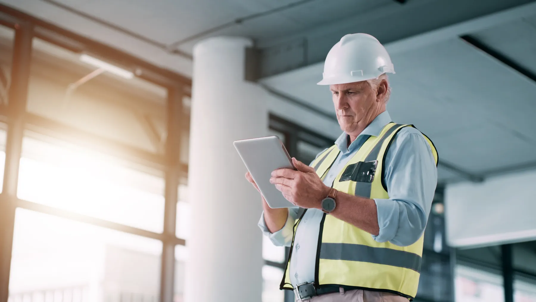 A man with hardhat uses a tablet inside a building space.