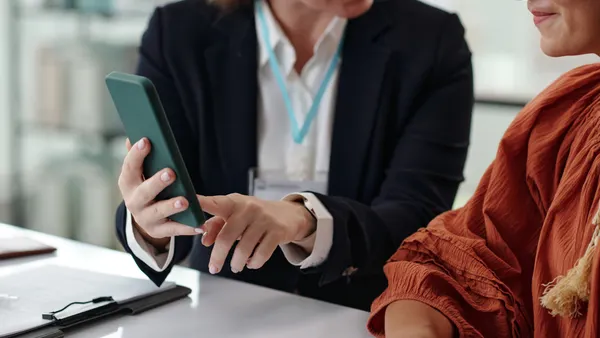 A person shows online registration to another person on mobile phone while they sitting in office
