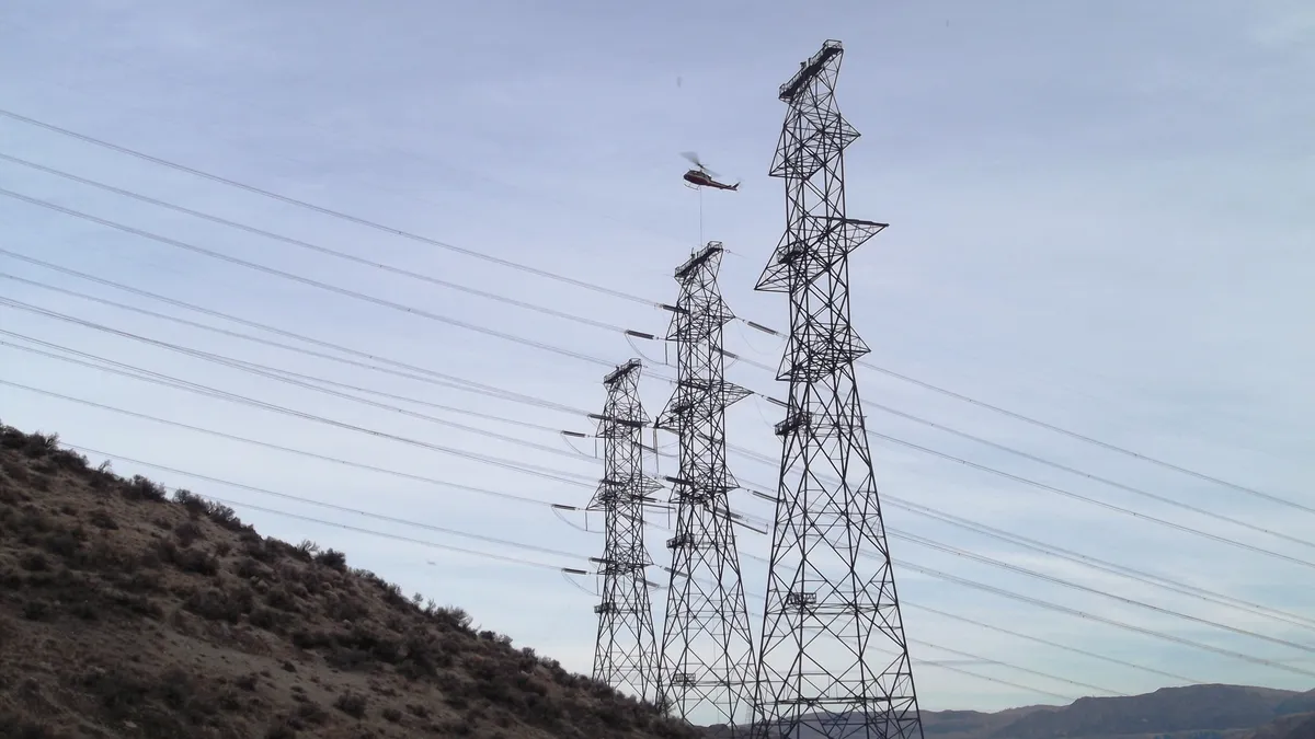 A helicopter hovers over transmission lines hung on three pylons.