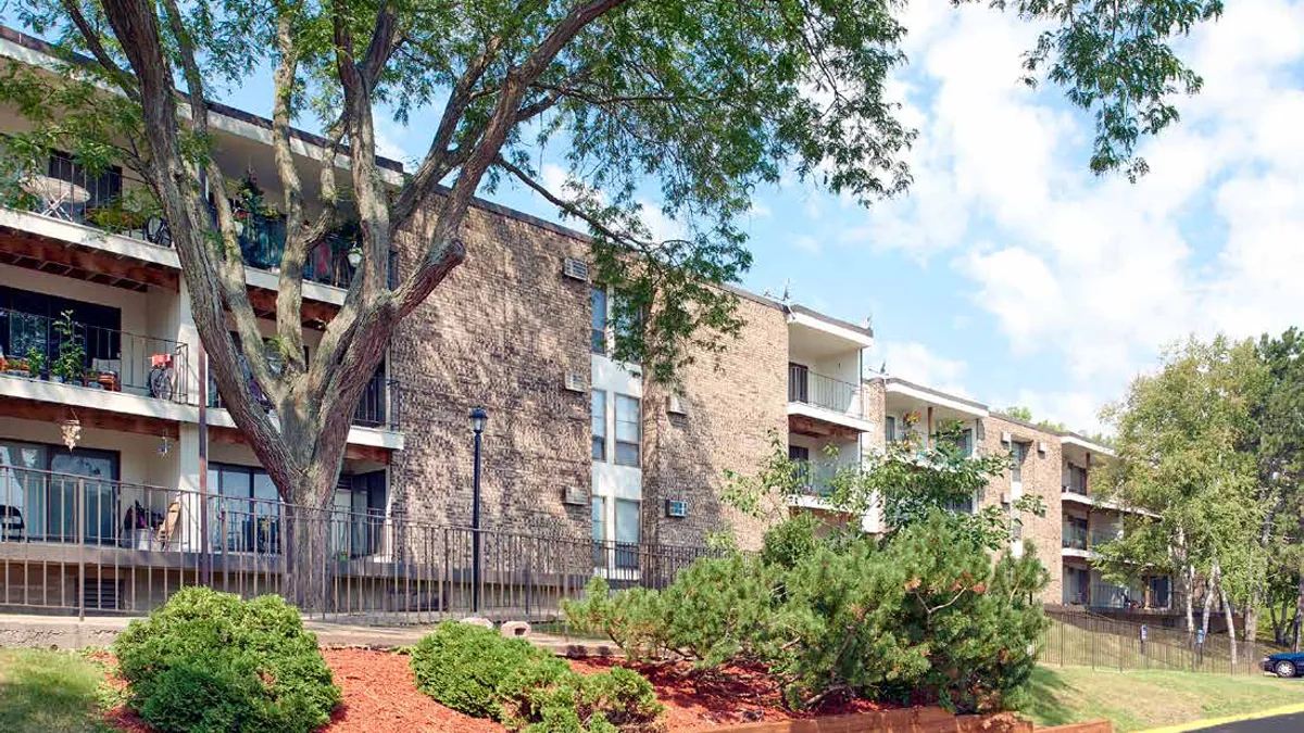 Three-story brick apartments with trees in the foreground.