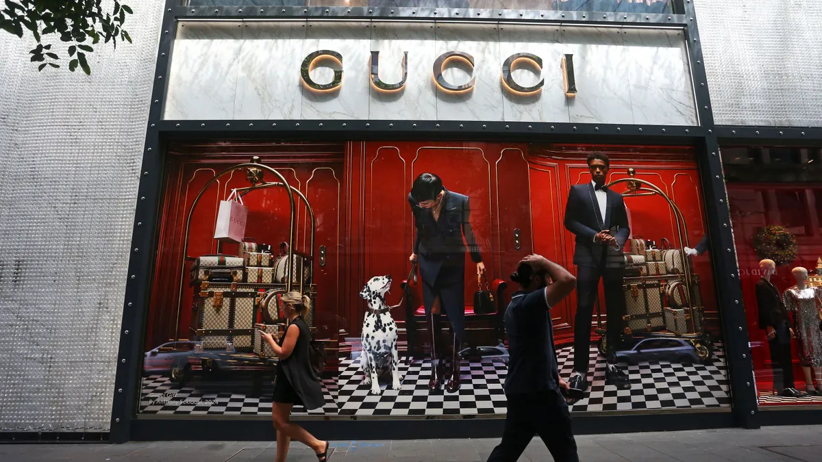 Pedestrians walk past a Gucci retail store window.