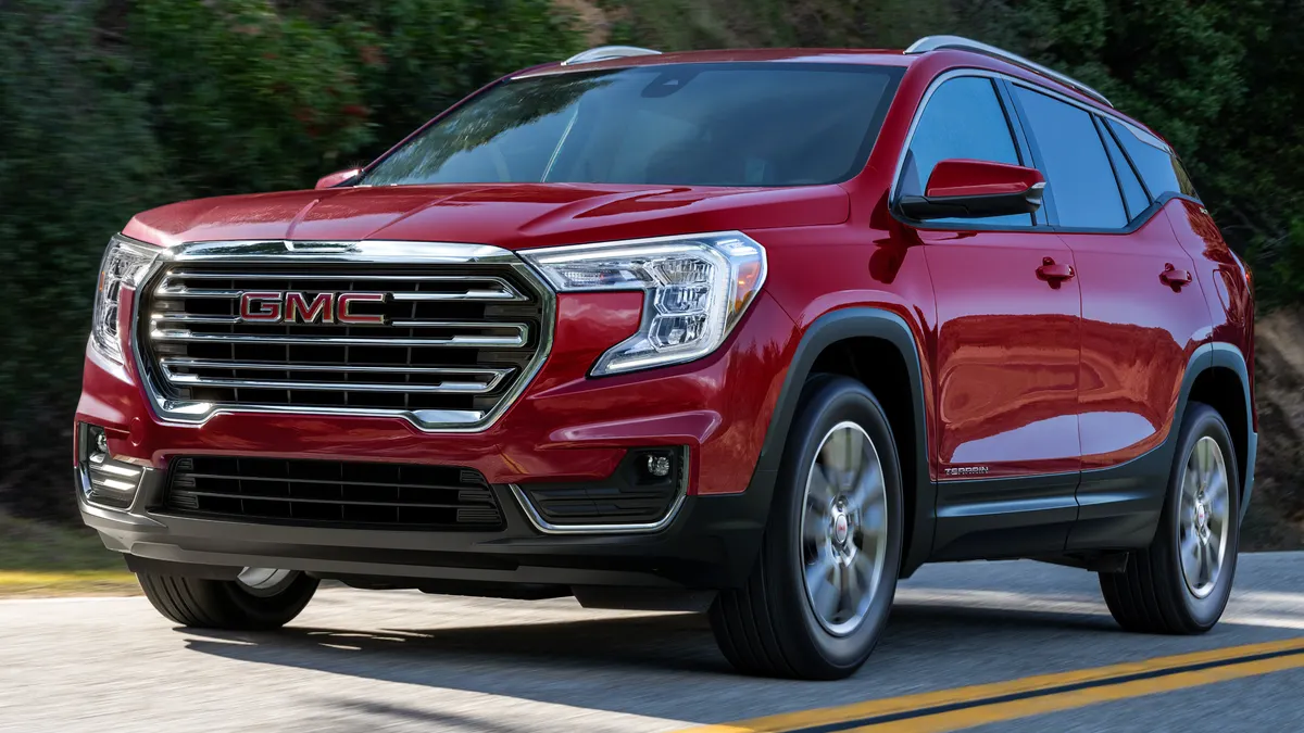 A red 2023 GMC Terrain SLT SUV driving on a road with greenery in the background.