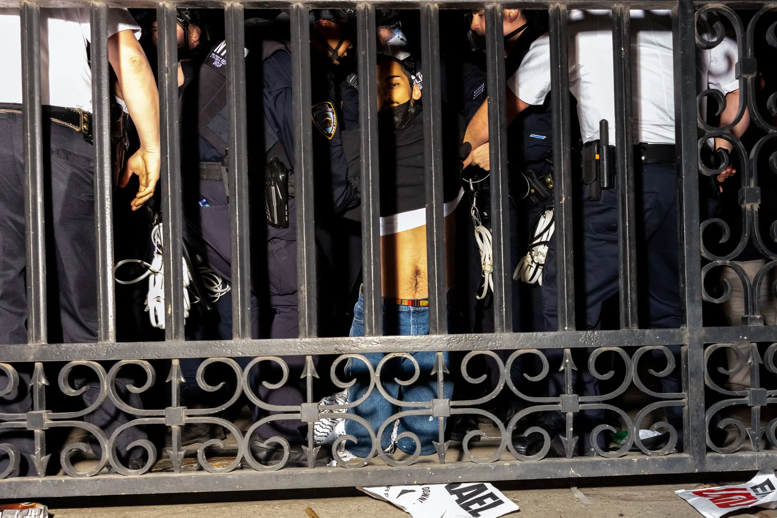 Two police officers grab each arm of a protester who is kneeling behind a fence.