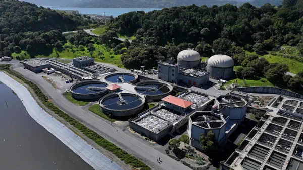 Aerial view of three round pools of water by a treatment plant.