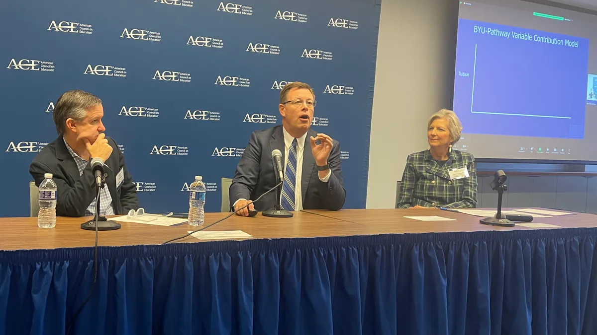 Three individuals sit a table discussing religious needs. A background with the American Council on Education logo is behind them.