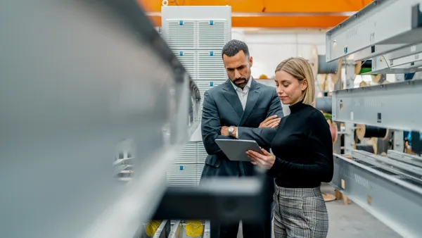 Businessman and woman with tablet at metal rods in factory hall