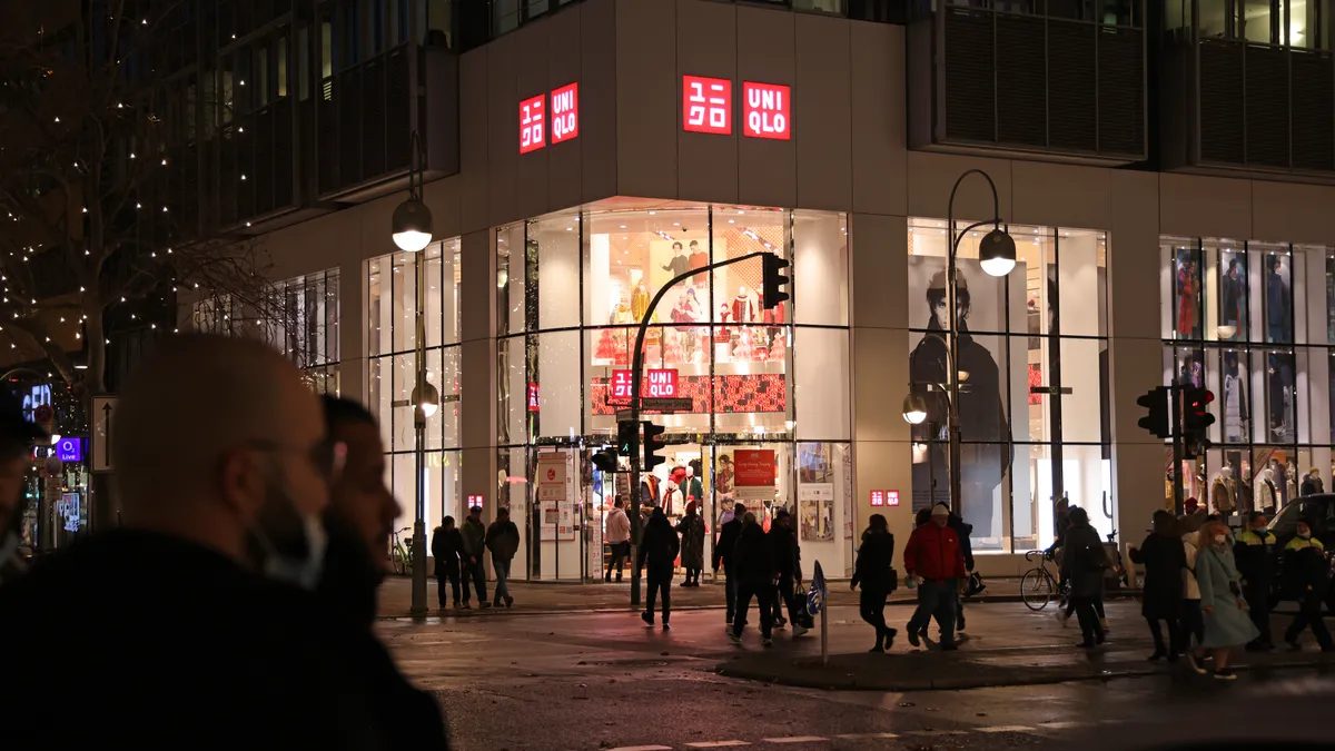 A Uniqlo store is pictured on the corner of a street in the evening while people walk past it.