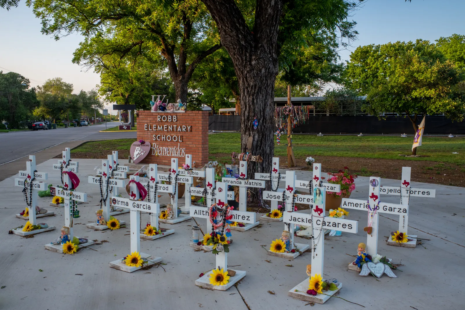 White crosses stand into front of a brick sign for Robb Elementary School.