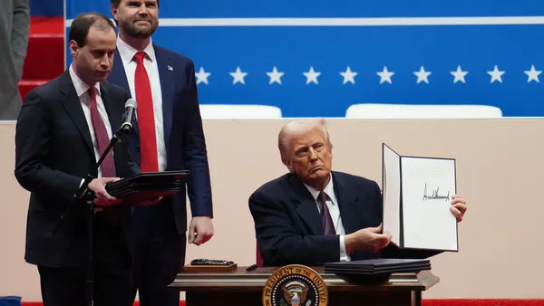 President Donald Trump holds up an executive order while two officials look on.