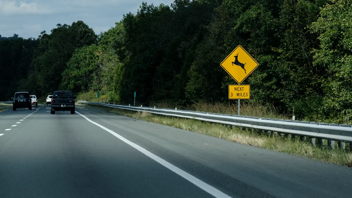 A sign alongside a divided highway warns drivers to be on the lookout for deer crossing the roadway.
