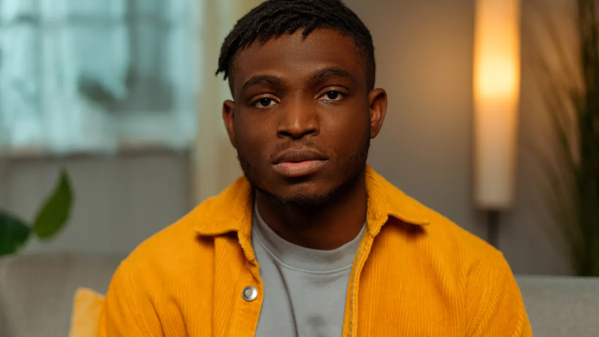 Portrait of pensive young African American person wearing yellow and looking at camera